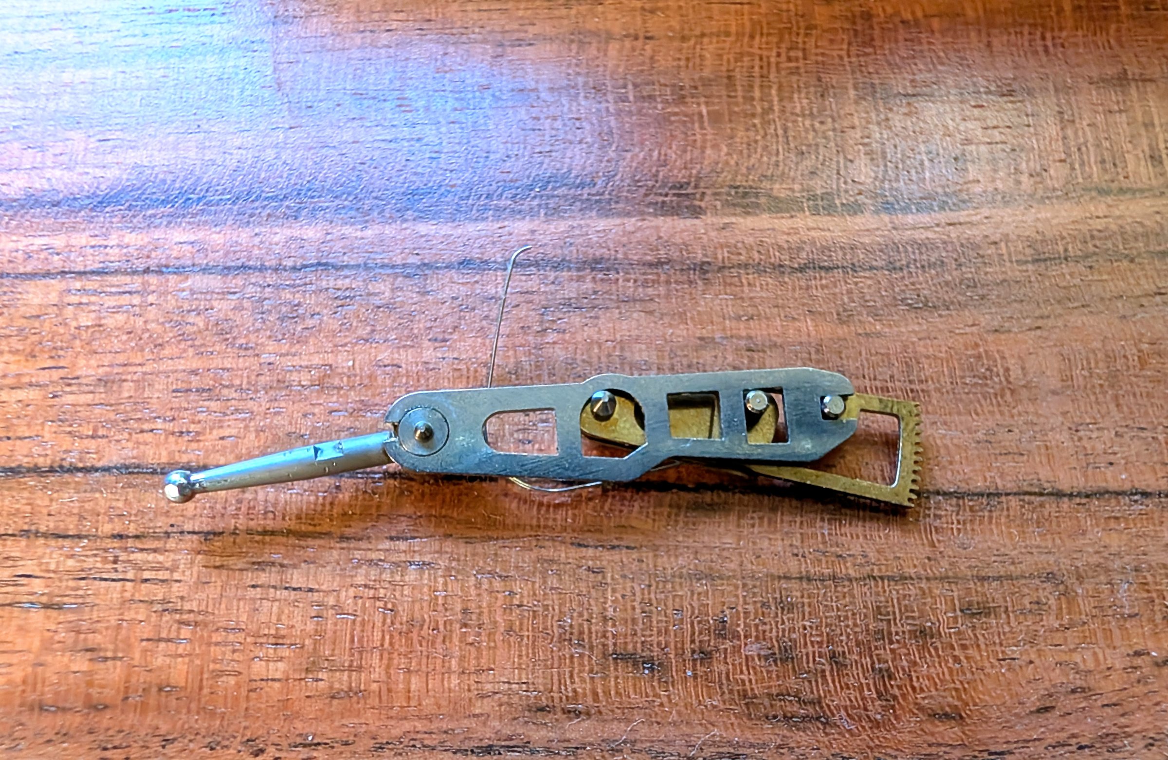 Lever assembly outside the body, correctly mated: steel contact-point lever over brass toothed rack, wire spring standing proud